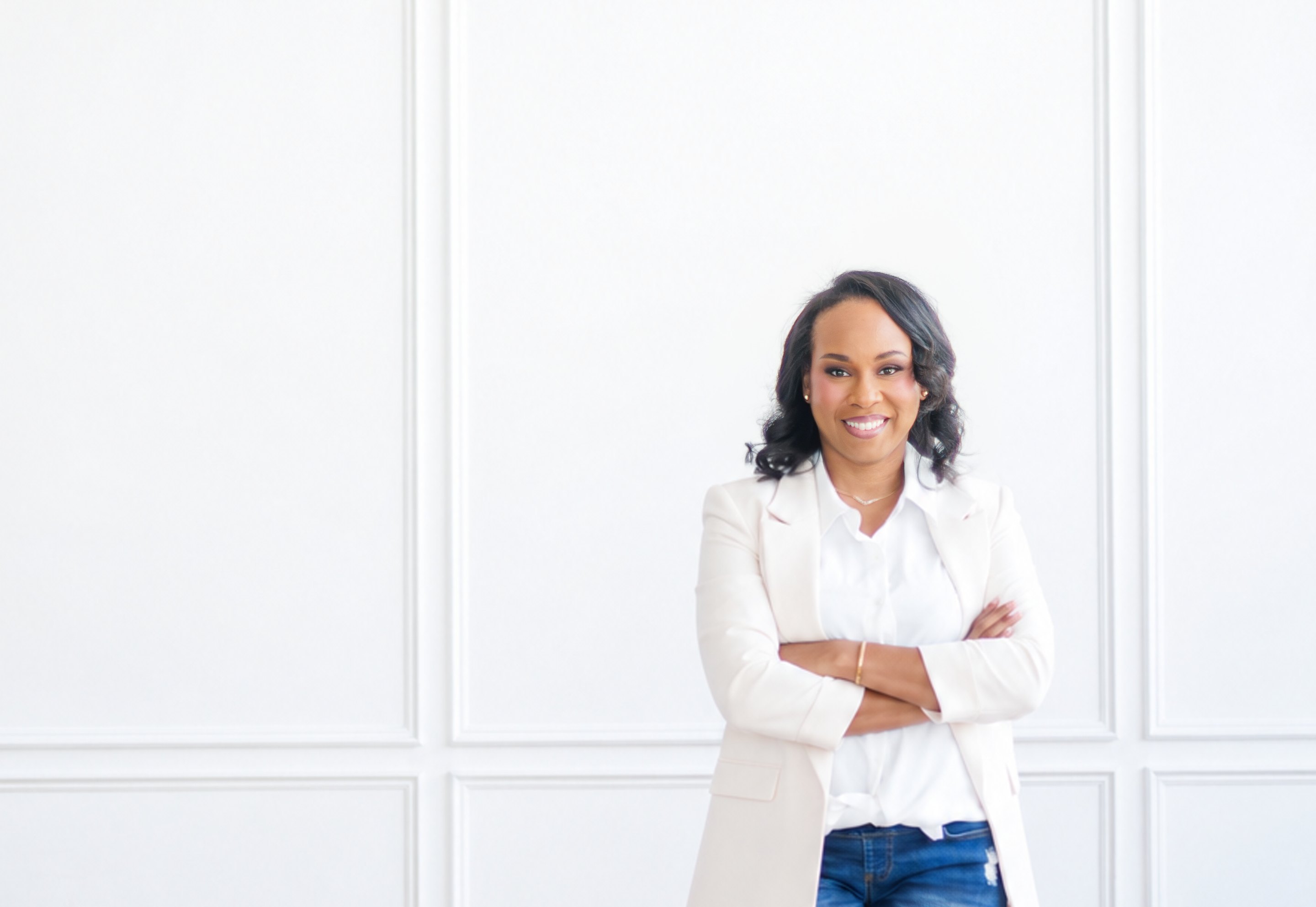 Amie Johnson in a white blazer, arms crossed, against a white paneled wall