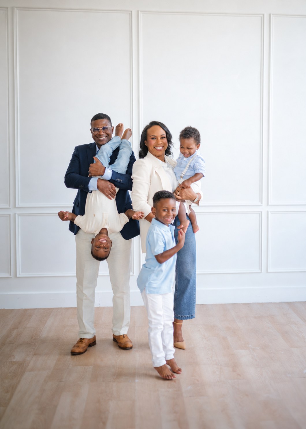 Amie with her husband and three sons in a white paneled studio, one son held playfully upside down